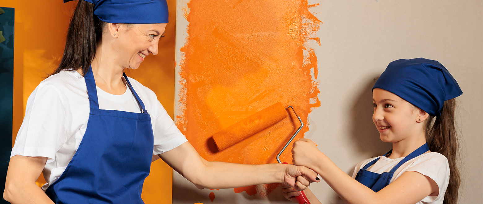 Menina ajudando sua mãe a pintar a parede com a cor laranja