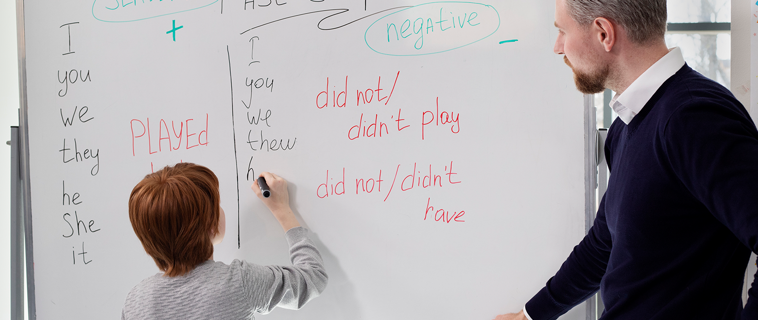 Professor auxiliando aluno a preencher o quadro com palavras em inglês.