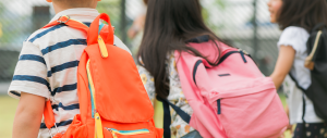 Visão de trás de crianças com mochilas indo em direção para a porta principal da escola