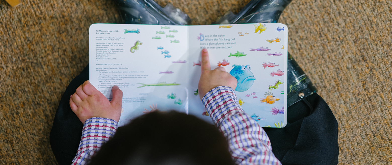Criança lendo um texto no caderno com desenhos de animais do mar.
