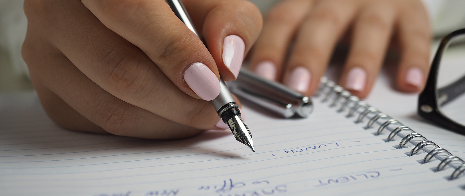 Imagem de uma mão escrevendo no caderno com uma caneta