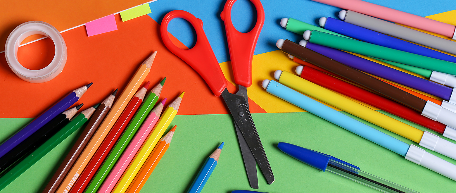 Vista de cima de uma mesa com vários materiais escolares coloridos e mãos manuseando as mesmas