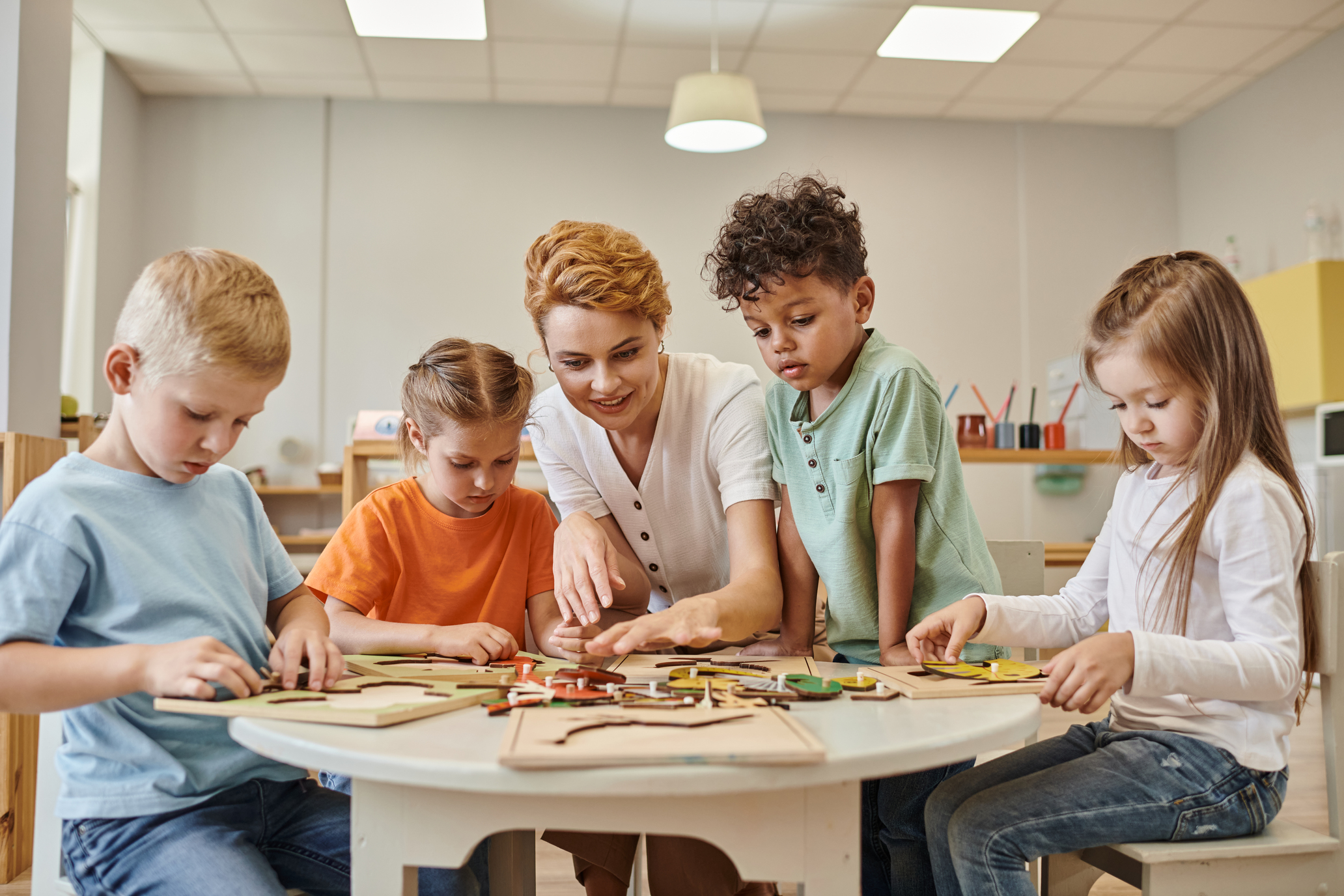 alunos ao redor da mesa com professora orientando uma atividade prática com peças em madeira